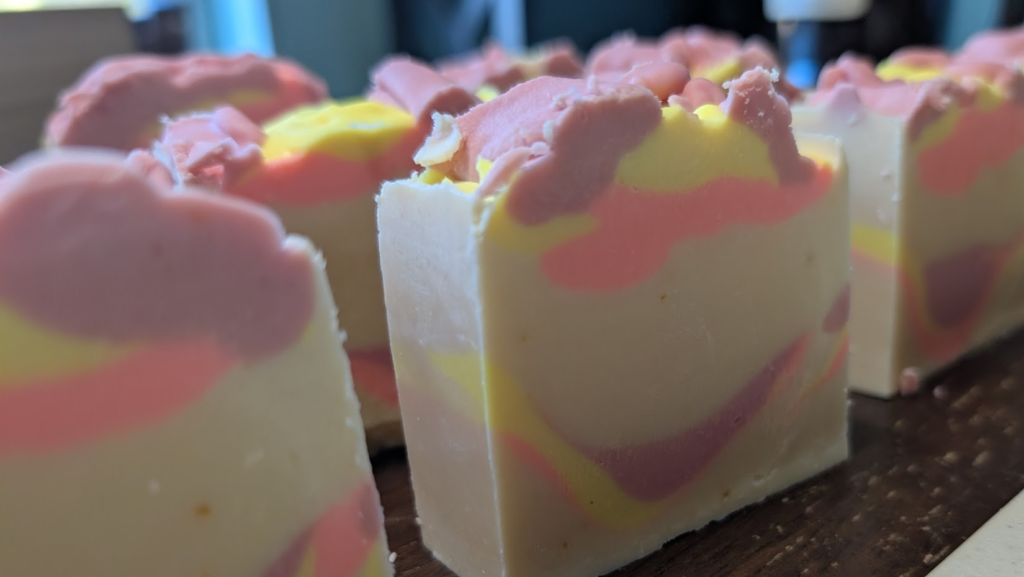 Bars of colorful homemade goat milk soap, a white base with yellow, purple, and pink swirled in.