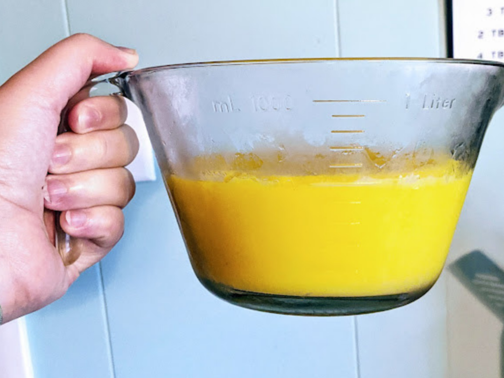 A hand holding a glass bowl full of a fresh batch of homemade lemon curd. 