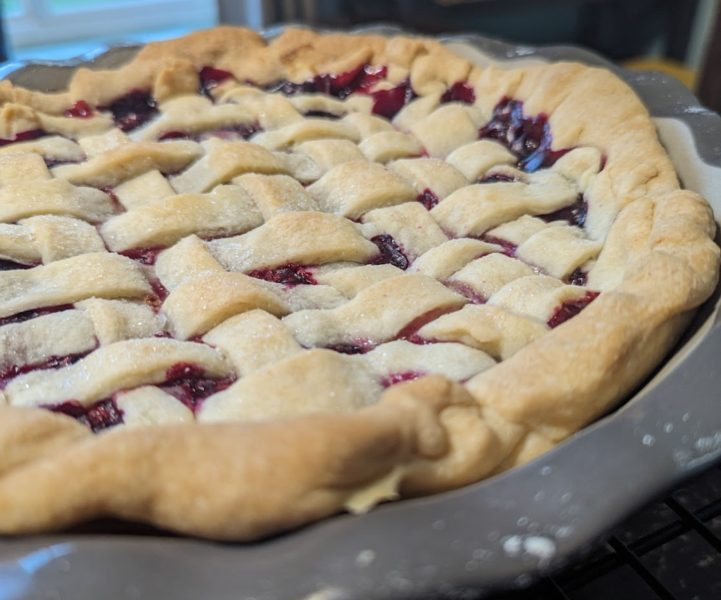 A freshly baked cherry pie with sugar dusted lattice crust in a grey scalloped pie plate. 